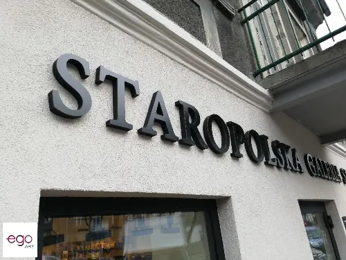Zbliżenie czarnych liter przestrzennych na jasnej elewacji restauracji.