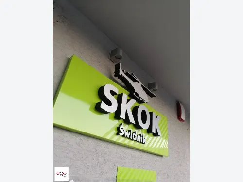 Wypukłe srebrne litery z ciemnymi bokami na zielonym szyldzie placówki SKOK.