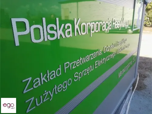 Zielony panel z wypukłymi srebrnymi napisami firmy i informacją o zakładzie przetwarzania sprzętu.