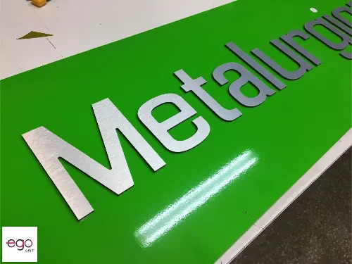 Zbliżenie srebrnych liter z metaliczną powierzchnią na błyszczącym zielonym tle.