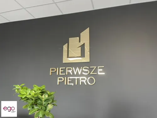 Złote lustrzane logo Pierwsze Piętro na ciemnej ścianie za recepcją.