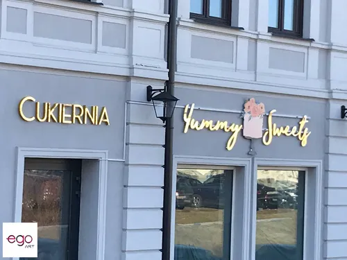 Złote lustrzane napisy nad drzwiami i witrynami cukierni, pokazane od frontu.