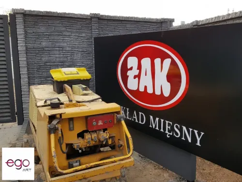 Czarny szyld zakładu mięsnego Żak przy ogrodzeniu