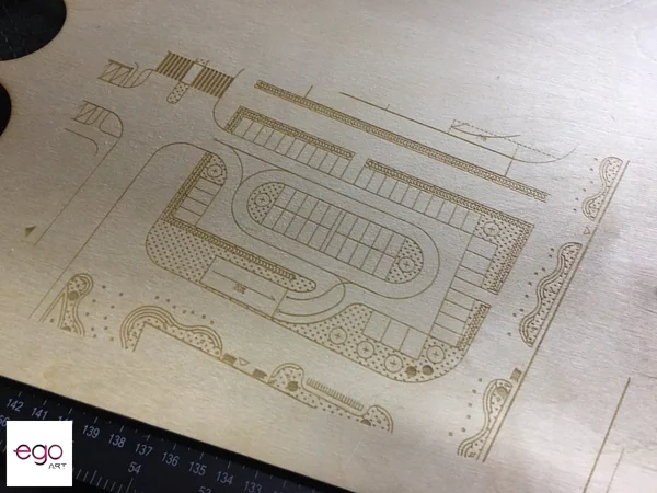 Precyzyjny grawer laserowy rysunku technicznego z detalami mechanicznymi na jasnej sklejce brzozowej.