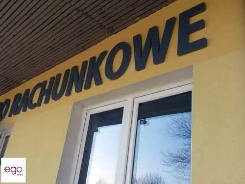 Ciemne litery przestrzenne nad oknem na żółtej elewacji biura rachunkowego.