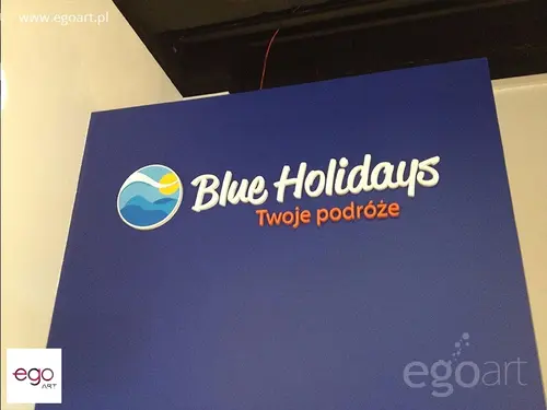 Biało-pomarańczowy napis Blue Holidays i okrągły znak na niebieskiej ścianie.