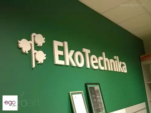 Jasne litery i znak drzewa EkoTechnika na zielonej ścianie w biurze.