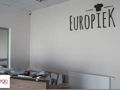 Czarne litery Europiek i symbol czapki kucharskiej na jasnej ścianie w biurze.