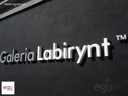 Białe litery przestrzenne Galeria Labirynt na ciemnej ścianie budynku.