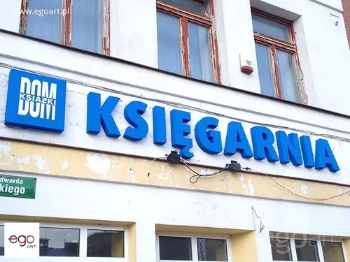 Duże niebieskie litery Księgarnia zamontowane na elewacji nad witrynami.