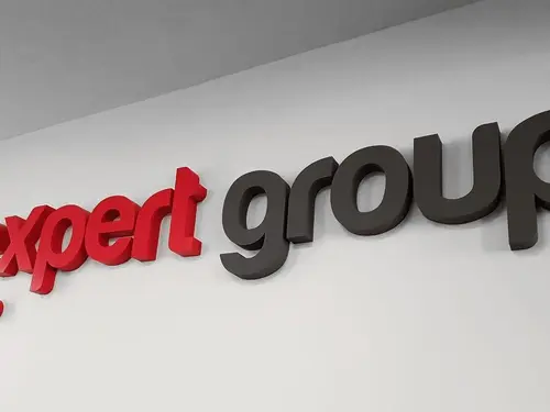 Czerwone i ciemnoszare litery logo Expert Group na jasnej ścianie.