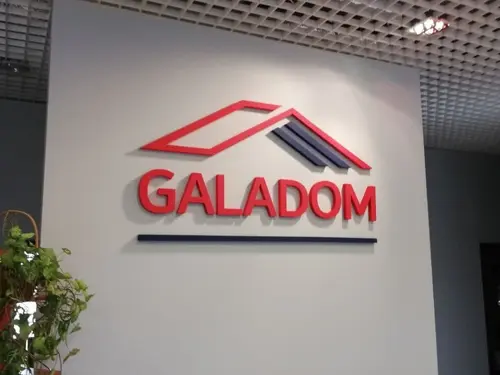 Czerwono-szare logo Galadom z motywem dachu na ścianie wewnątrz biura.