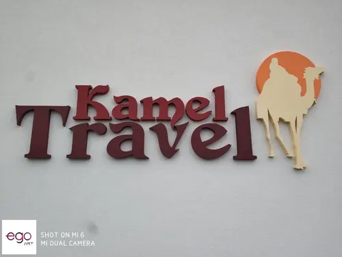 Bordowe litery Kamel Travel i jasny znak wielbłąda z malowanego styroduru na ścianie.