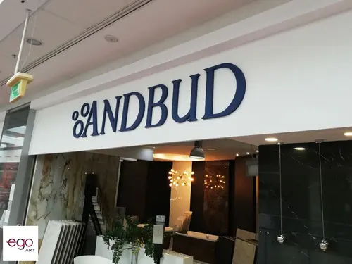 Granatowy napis Andbud na białym panelu nad wejściem do salonu w galerii handlowej.