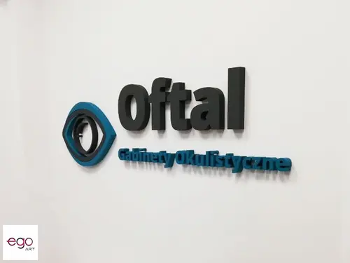 Czarno-niebieskie logo Oftal i napis Gabinety okulistyczne na jasnej ścianie.