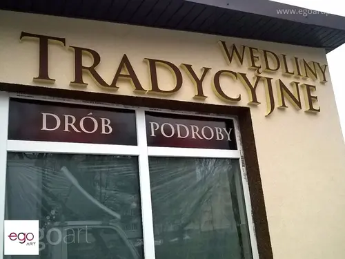 Brązowe litery przestrzenne Wędliny tradycyjne nad witryną sklepu.