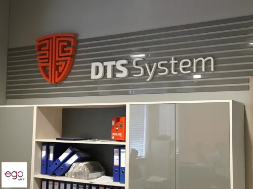 Pomarańczowy znak i białe litery DTS System na pasiastej ścianie nad zabudową biurową.