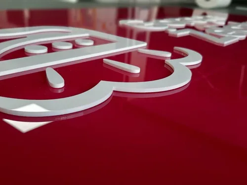 Zbliżenie białego logo wyciętego z plexi na czerwonym tle z widoczną grubością materiału.