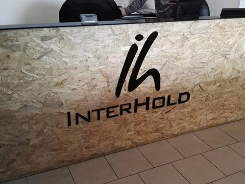 Czarny znak i napis Interhold na drewnopochodnej płycie frontu lady recepcyjnej.