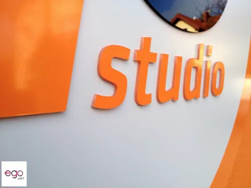 Zbliżenie pomarańczowego napisu Studio z plexi na białym okrągłym tle.