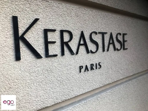 Czarny napis Kérastase Paris wycięty z plexi i zamontowany na jasnej ścianie.