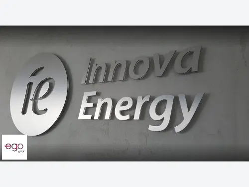 Srebrne logo Innova Energy ze szczotkowanym licem i ciemnymi bokami na szarej ścianie.