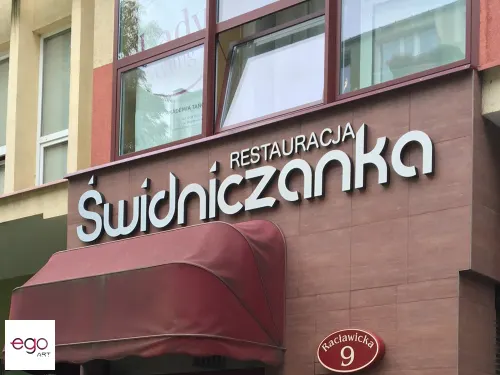 Przestrzenny napis Restauracja Świdniczanka nad wejściem z bordowym daszkiem.