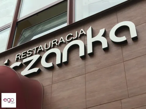 Zbliżenie liter restauracji Świdniczanka ze srebrnym licem i ciemnymi bokami na elewacji.