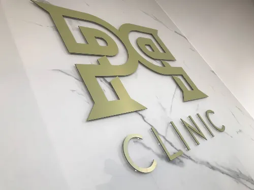 Złoty geometryczny znak i napis Clinic ze szczotkowanego dibondu na tle z marmurowym wzorem.
