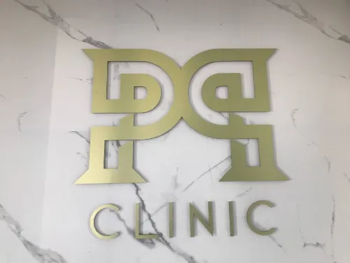 Złote logo kliniki i litery Clinic na jasnej ścianie z szarym użyleniem.
