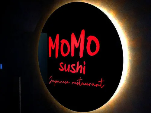 Okrągłe logo Momo Sushi — efekt aureoli na ścianie