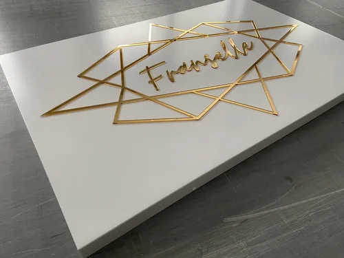 Złoty napis i geometryczna oprawa logo na białym przestrzennym panelu z dibondu.