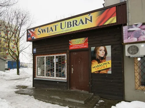 Żółty szyld Świat Ubrań oraz grafiki reklamowe na elewacji sklepu odzieżowego.