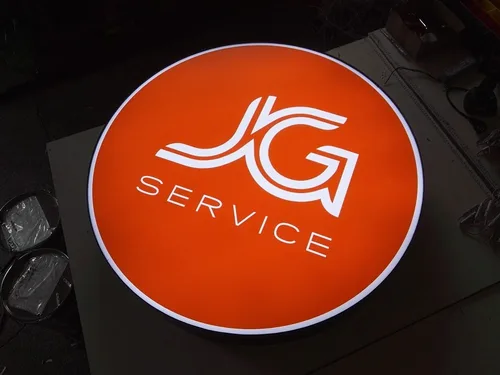 Pomarańczowy okrągły kaseton z białym logo JG Service i jasną obwódką.