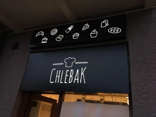 Czarny matowy kaseton z dibondu z białym logo Chlebak i piktogramami pieczywa nad wejściem.