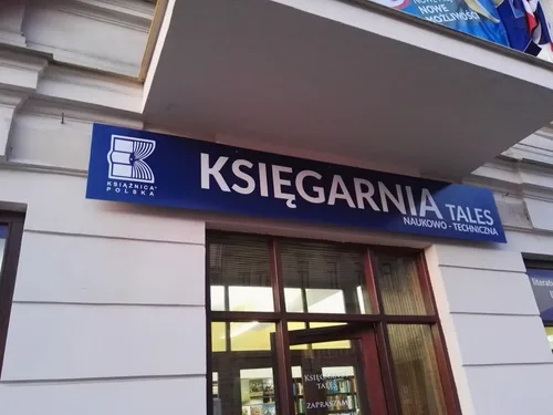 Niebieska plansza z dibondu z białym napisem Księgarnia, zamontowana nad wejściem do sklepu.