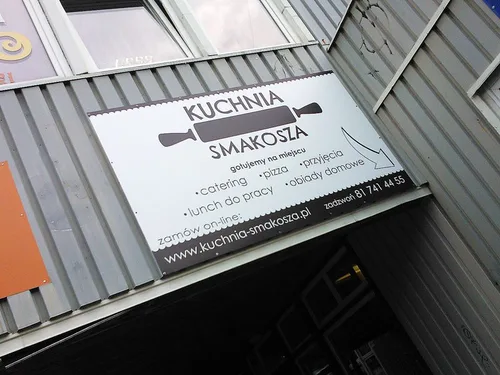 Biała plansza Kuchnia Smakosza z logo, zakresem usług i danymi kontaktowymi nad wejściem.