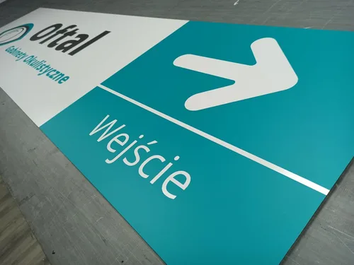 Tablica z dibondu z turkusowym polem, białą strzałką i napisem Wejście wykonanym z folii.