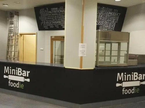 Czarne plansze z PCV z białym logo MiniBar, zamontowane na froncie lady gastronomicznej.