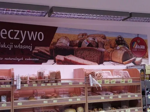 Ścienna plansza z PCV z grafiką pieczywa, zamontowana nad półkami sklepowymi.