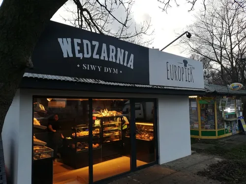 Szyldy z dibondu z oznaczeniami Wędzarnia i Europiek nad witryną sklepu spożywczego.