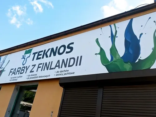 Duży szyld z dibondu z kolorową grafiką farb, zamocowany na konstrukcji przy budynku.