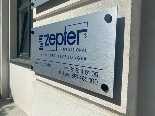 Srebrna tabliczka z niebieskim logo Zepter, zamontowana na czterech czarnych dystansach.
