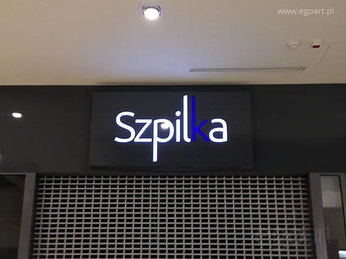 Grafitowy kaseton z dibondu z jasnym napisem Szpilka nad wejściem do sklepu.