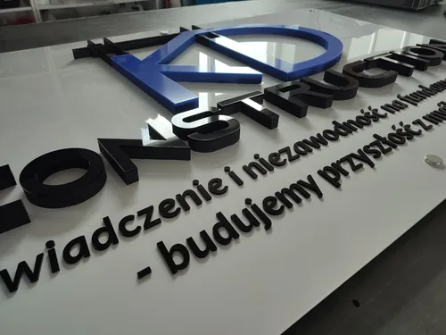 Tablica na dystansach z niebieskim znakiem i czarnymi literami przestrzennymi.