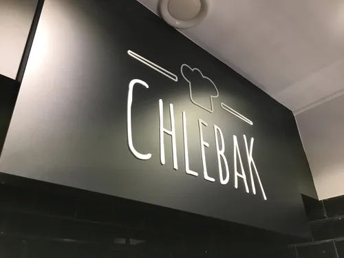 Czarny szyld Chlebak z białym logo i literami z plexi nad wejściem do lokalu.