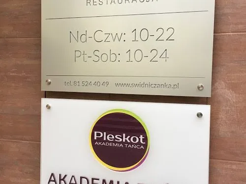 Dwie jasne tablice z plexi na dystansach z oznaczeniem lokalu i godzinami otwarcia.