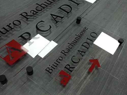 Przezroczysta tablica z czarno-czerwonym logo Arcadio i czarnymi dystansami.