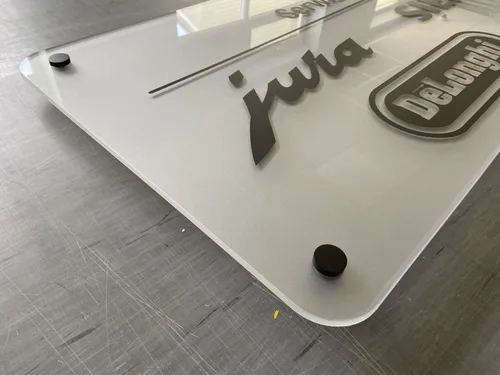 Zbliżenie tablicy z mrożonej plexi z zaokrąglonym narożnikiem, czarnym dystansem i logotypami.