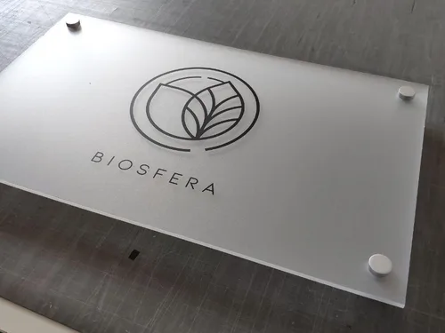 Tablica z matowej mrożonej plexi z czarnym logo Biosfera i srebrnymi dystansami.